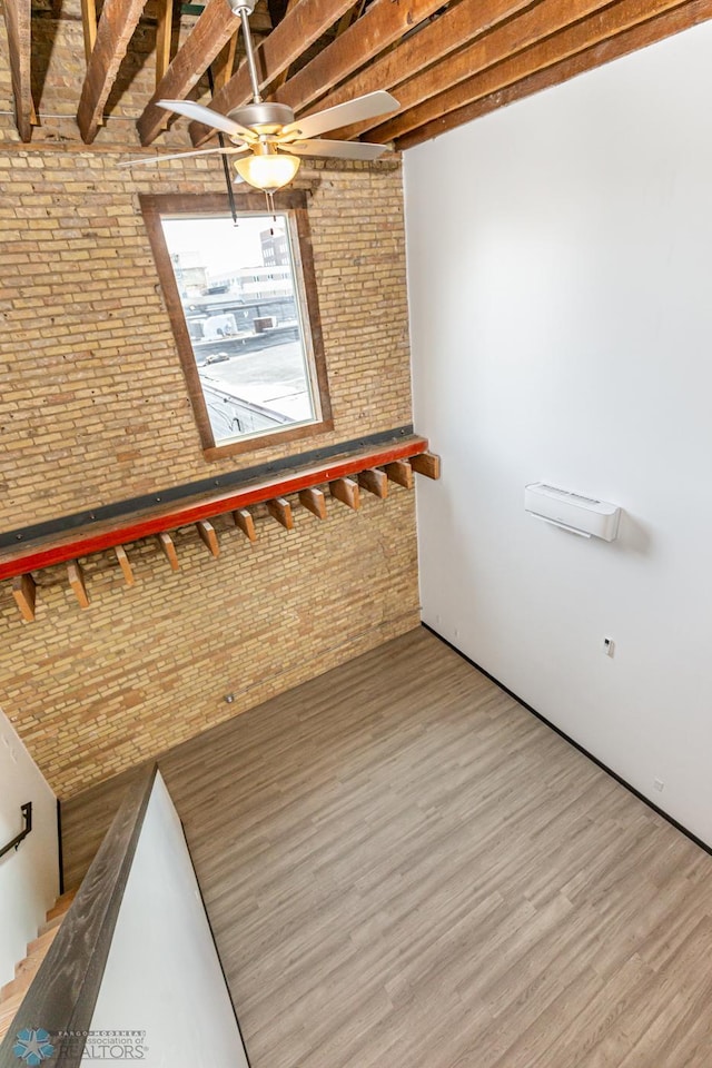 interior space with a ceiling fan, beamed ceiling, brick wall, and wood finished floors