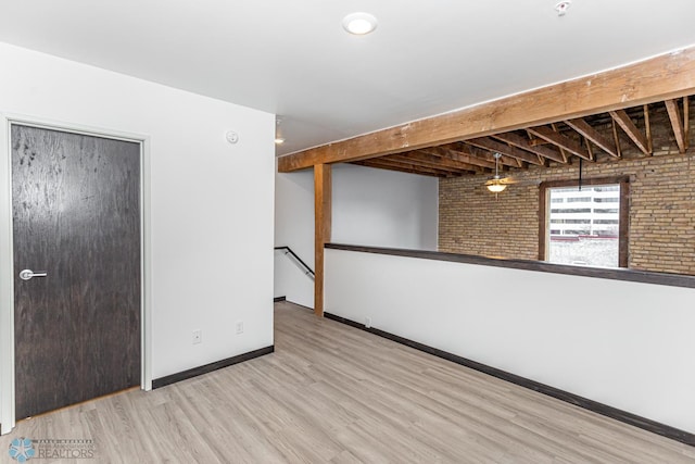 empty room with brick wall, beamed ceiling, wood finished floors, and baseboards