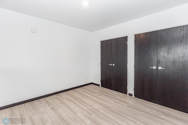 unfurnished bedroom featuring baseboards, two closets, and wood finished floors