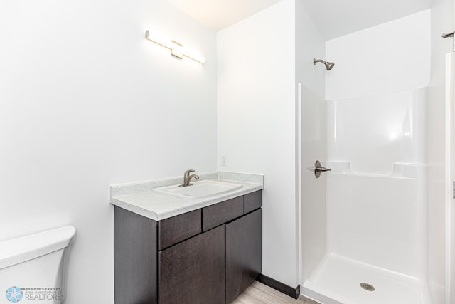 bathroom with wood finished floors, vanity, toilet, and walk in shower