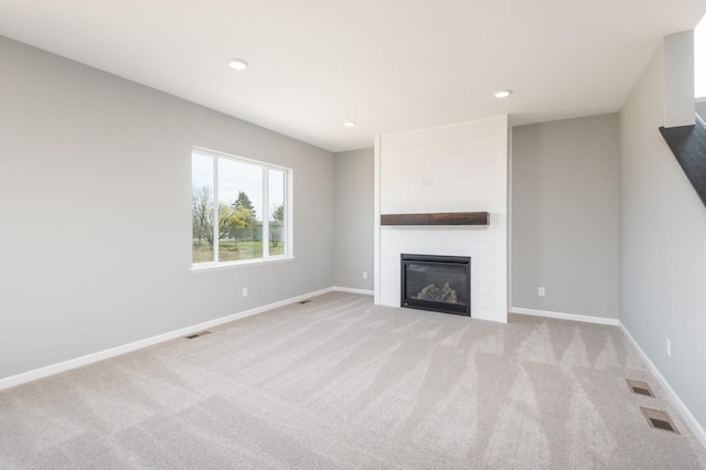 unfurnished living room featuring light carpet and a large fireplace