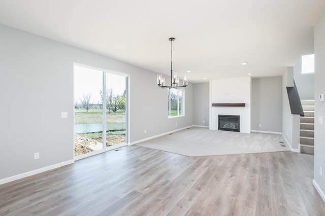 unfurnished living room with a large fireplace, a chandelier, and light hardwood / wood-style flooring