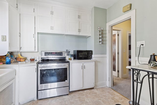 kitchen with stainless steel range with electric stovetop, light carpet, and white cabinets