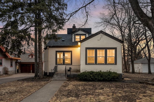 view of front of home with stucco siding, driveway, a chimney, and a shingled roof