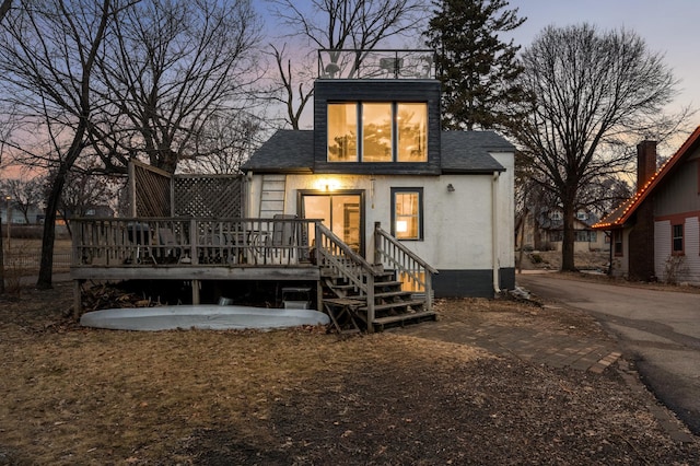 back of property with stucco siding, roof with shingles, a deck, and driveway