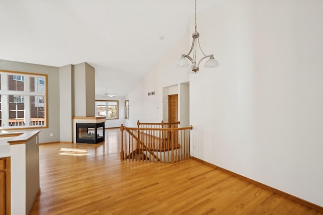 living room with ceiling fan with notable chandelier, a multi sided fireplace, high vaulted ceiling, and light wood-type flooring