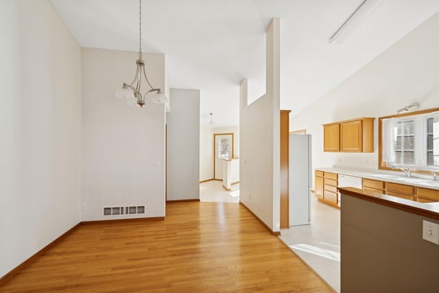 kitchen with sink, vaulted ceiling, hanging light fixtures, white appliances, and light hardwood / wood-style floors