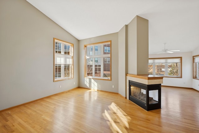 unfurnished room with vaulted ceiling, a multi sided fireplace, light wood-style flooring, and baseboards