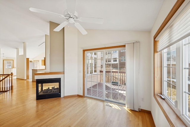 interior space featuring a multi sided fireplace, a ceiling fan, baseboards, vaulted ceiling, and light wood-style floors