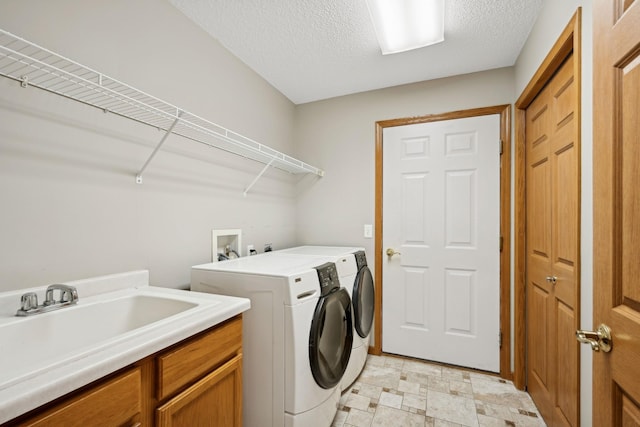 washroom with a textured ceiling, a sink, washer and dryer, cabinet space, and light floors