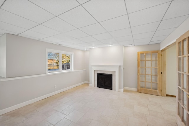 unfurnished living room with a paneled ceiling, baseboards, and a tiled fireplace