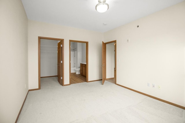 unfurnished bedroom featuring a spacious closet, ensuite bath, light colored carpet, and a closet