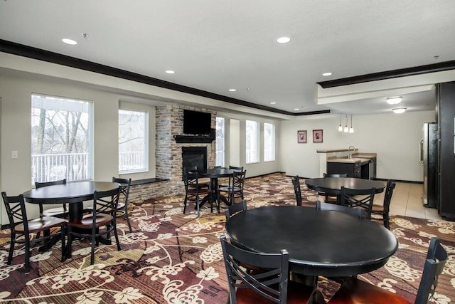 tiled dining space with crown molding, a stone fireplace, sink, and a wealth of natural light