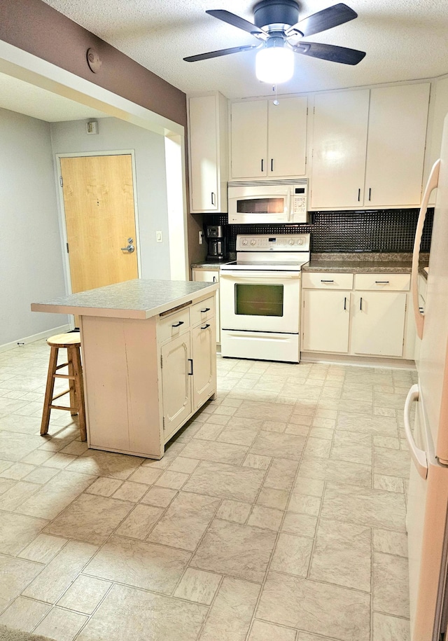 kitchen with a kitchen breakfast bar, a textured ceiling, white appliances, ceiling fan, and a kitchen island