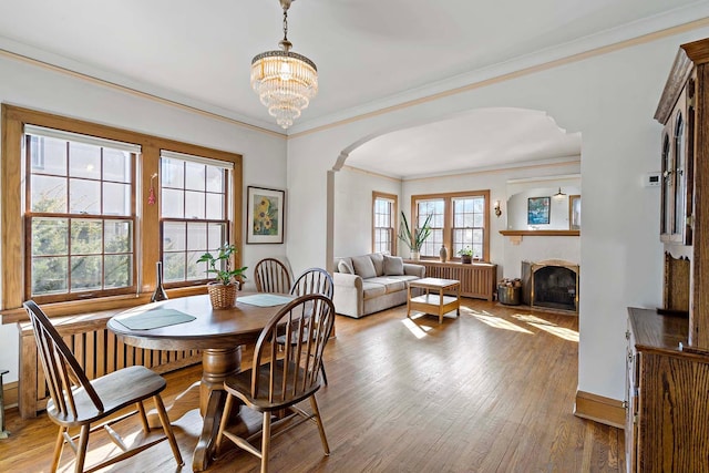 dining space featuring radiator, an inviting chandelier, a fireplace, arched walkways, and light wood-style floors