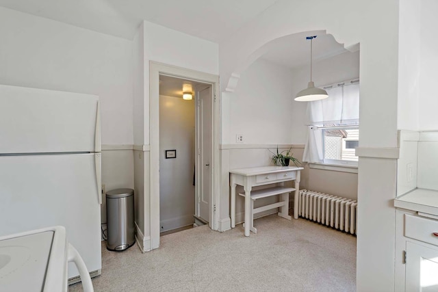 kitchen with radiator, light carpet, freestanding refrigerator, stove, and white cabinets