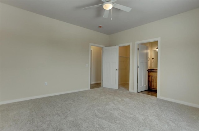 unfurnished bedroom featuring ensuite bath, ceiling fan, a walk in closet, light colored carpet, and a closet