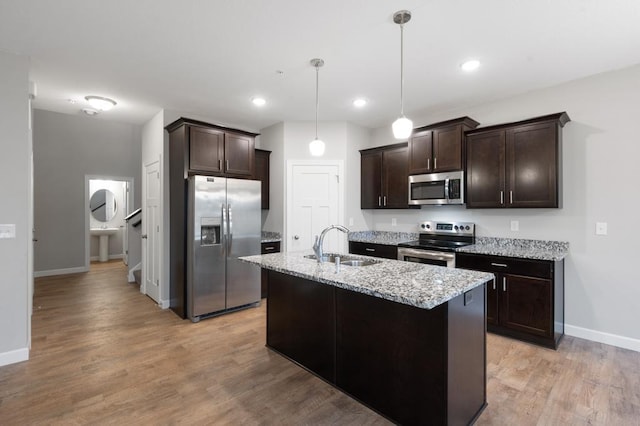 kitchen with a kitchen island with sink, hanging light fixtures, sink, light stone counters, and stainless steel appliances