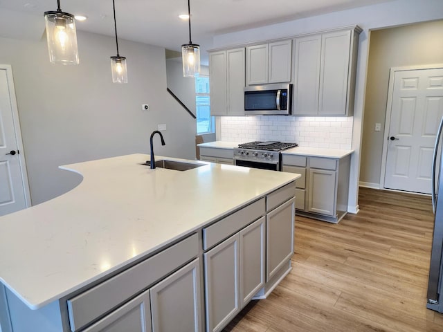 kitchen with backsplash, pendant lighting, a center island with sink, sink, and stainless steel appliances