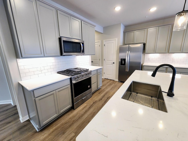 kitchen with decorative backsplash, appliances with stainless steel finishes, gray cabinetry, and pendant lighting