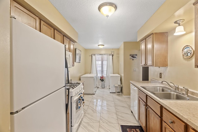 kitchen featuring sink, white appliances, a textured ceiling, and washing machine and dryer