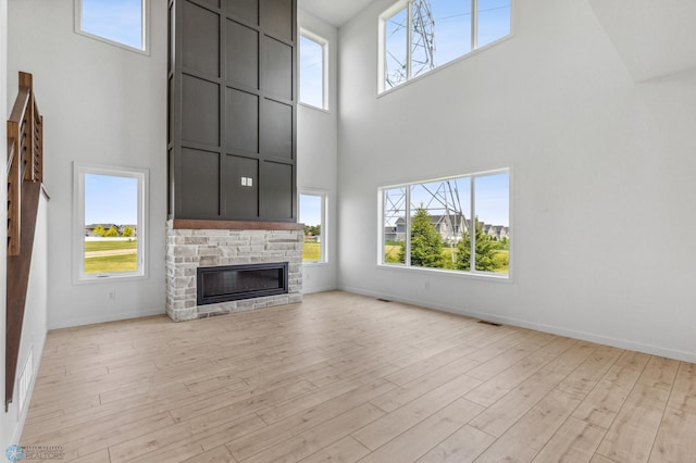 unfurnished living room featuring a fireplace, a towering ceiling, and light wood-type flooring