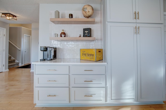 bar with tasteful backsplash, white cabinets, a textured ceiling, and light hardwood / wood-style floors