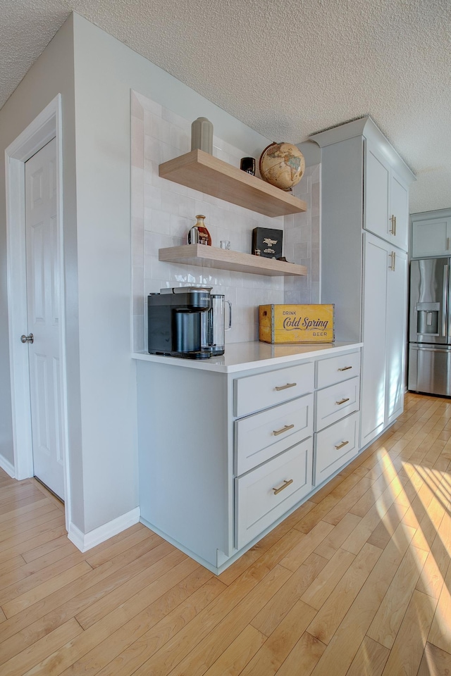 kitchen featuring white cabinetry, stainless steel fridge, decorative backsplash, light hardwood / wood-style floors, and a textured ceiling