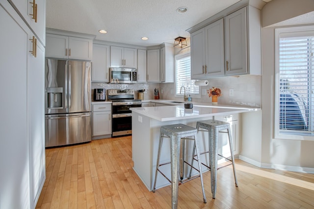 kitchen featuring sink, a breakfast bar area, tasteful backsplash, light wood-type flooring, and appliances with stainless steel finishes