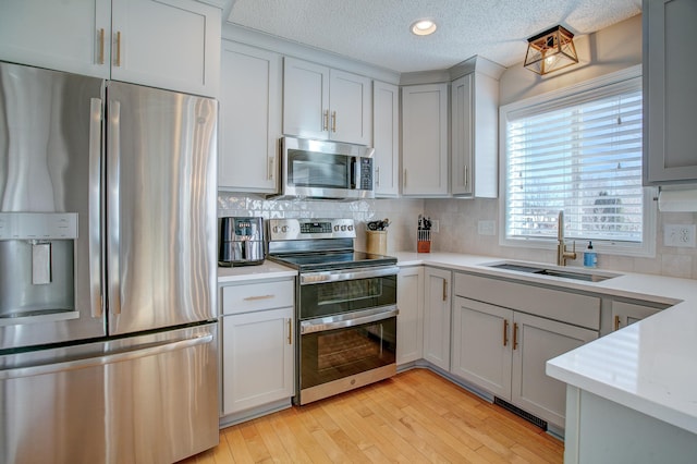 kitchen with sink, stainless steel appliances, tasteful backsplash, light hardwood / wood-style floors, and a textured ceiling