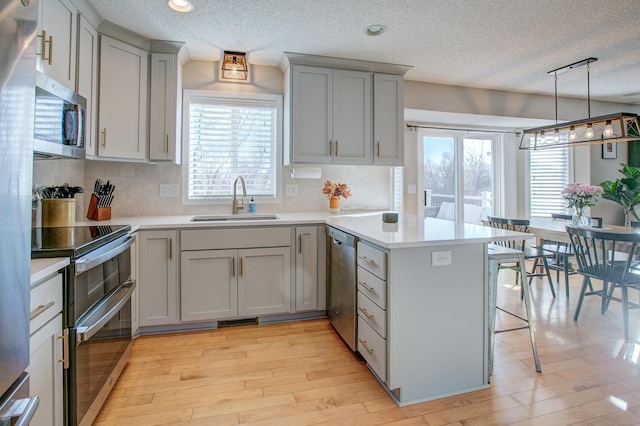 kitchen with sink, appliances with stainless steel finishes, a kitchen breakfast bar, decorative light fixtures, and kitchen peninsula