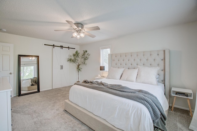 bedroom with ceiling fan, a barn door, light colored carpet, and a textured ceiling