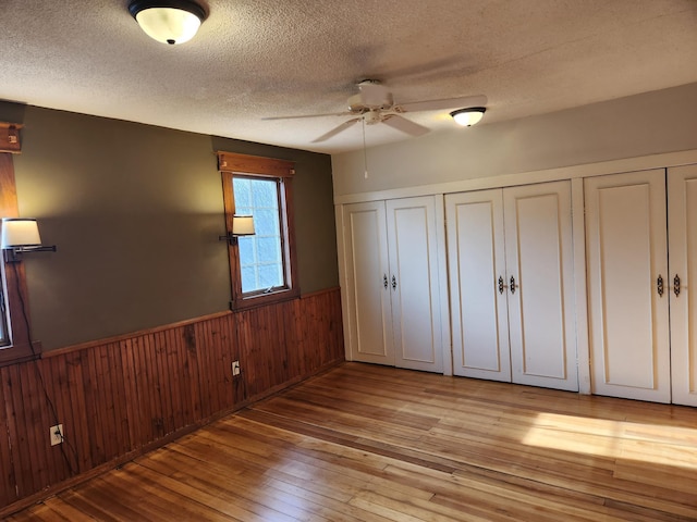 unfurnished bedroom with wood walls, light hardwood / wood-style flooring, ceiling fan, and a textured ceiling