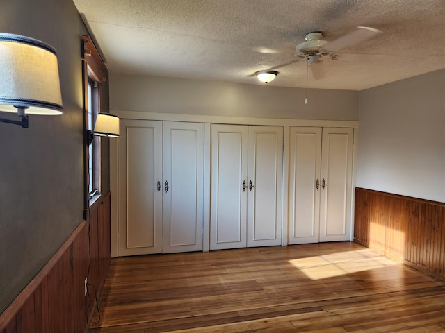 unfurnished bedroom with a textured ceiling, hardwood / wood-style flooring, ceiling fan, and wooden walls