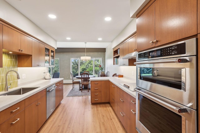 kitchen featuring kitchen peninsula, appliances with stainless steel finishes, sink, decorative light fixtures, and light hardwood / wood-style floors