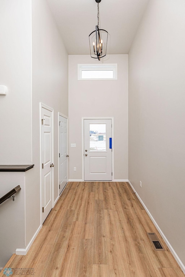 doorway featuring a notable chandelier, a towering ceiling, and light hardwood / wood-style flooring