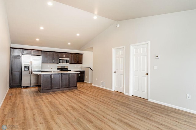 kitchen featuring lofted ceiling, stainless steel appliances, an island with sink, light hardwood / wood-style flooring, and dark brown cabinets