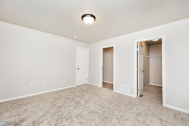 unfurnished bedroom featuring a spacious closet, a closet, and light carpet