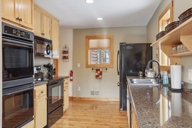 kitchen featuring light brown cabinets, dark stone counters, black appliances, sink, and light wood-type flooring