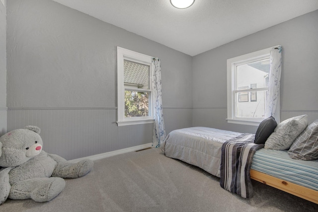 carpeted bedroom with a wainscoted wall and a textured ceiling