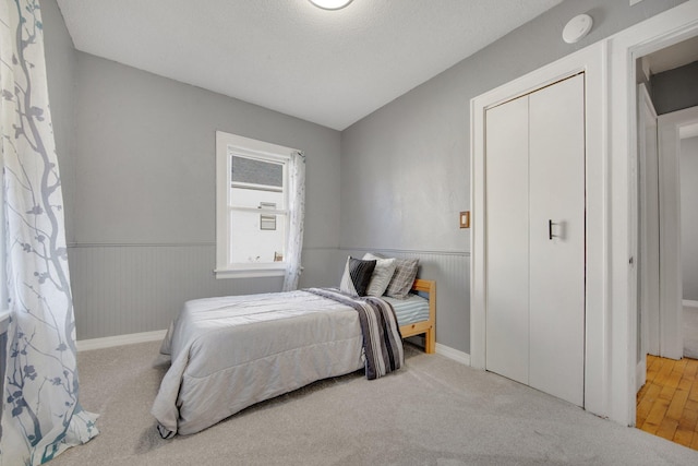 bedroom featuring a textured ceiling, carpet floors, a closet, and wainscoting