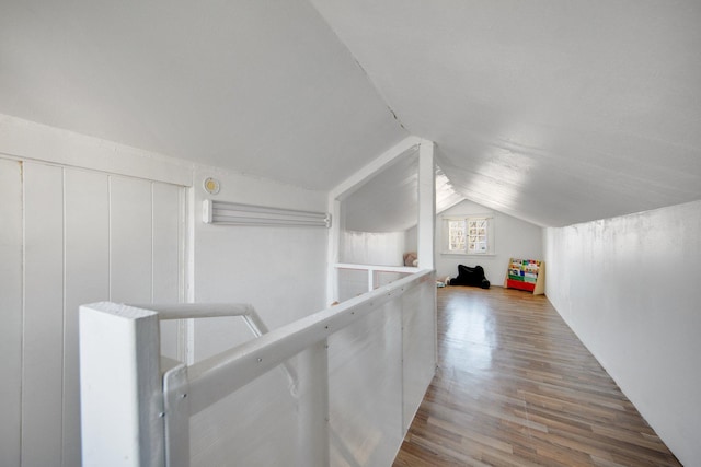 corridor with vaulted ceiling, wood finished floors, and an upstairs landing