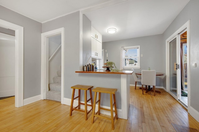 kitchen featuring baseboards, white cabinets, a kitchen breakfast bar, a peninsula, and light wood-type flooring