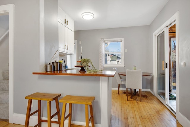 kitchen with a kitchen bar, white cabinetry, light wood-type flooring, a peninsula, and baseboards