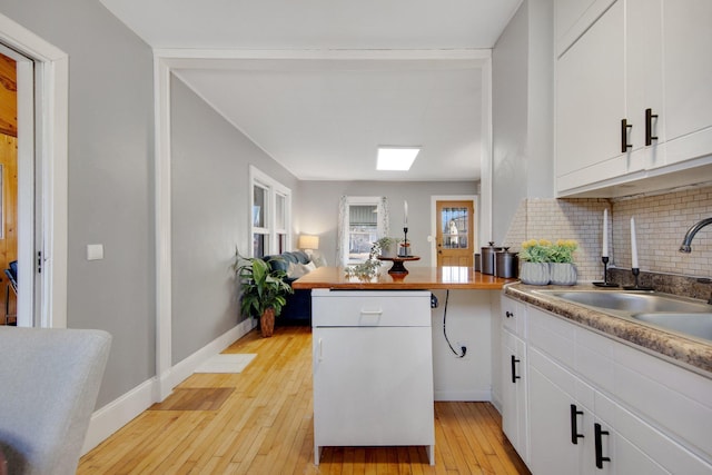 kitchen featuring a sink, decorative backsplash, light wood finished floors, a peninsula, and white cabinetry