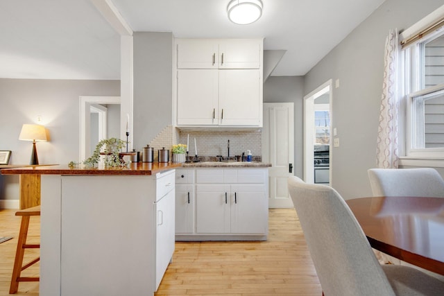kitchen featuring light wood-style floors, backsplash, a sink, a breakfast bar area, and healthy amount of natural light