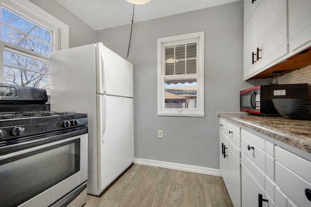 kitchen with stainless steel gas range oven, black microwave, light wood-style floors, baseboards, and white cabinetry