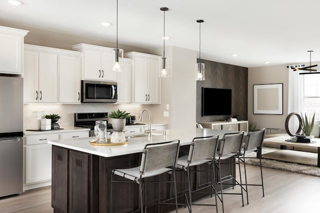 kitchen featuring white cabinetry, stainless steel appliances, pendant lighting, a center island with sink, and light wood-type flooring