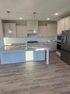 kitchen featuring pendant lighting, a center island with sink, light wood-type flooring, and stainless steel refrigerator