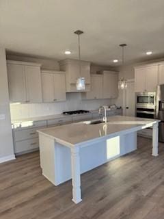 kitchen with stainless steel appliances, a center island with sink, hanging light fixtures, and dark hardwood / wood-style floors